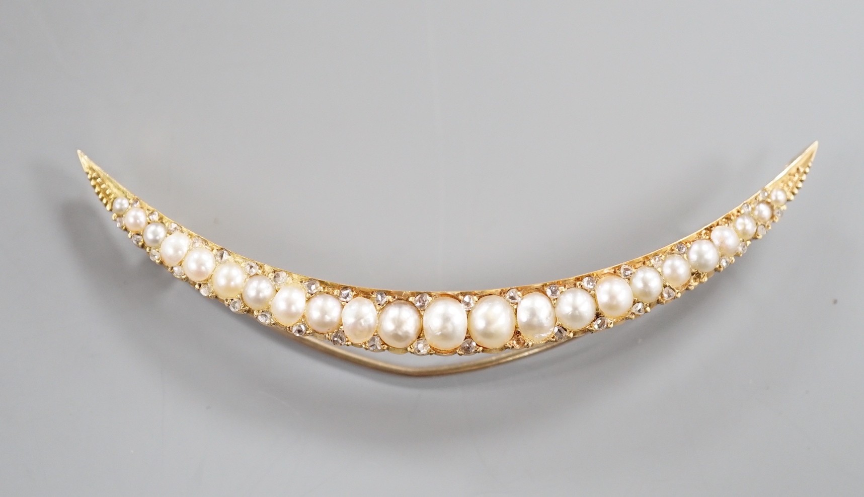 An early 20th century yellow metal and graduated split pearl set crescent brooch, with diamond chip spacers, 8cm, gross weight 8.1 grams.